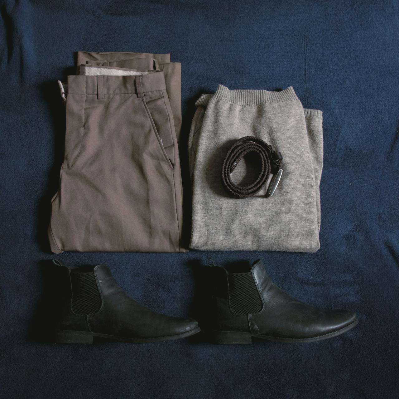 heros-img Men's clothing ensemble including trousers, sweater, boots, and belt arranged on a blue surface.