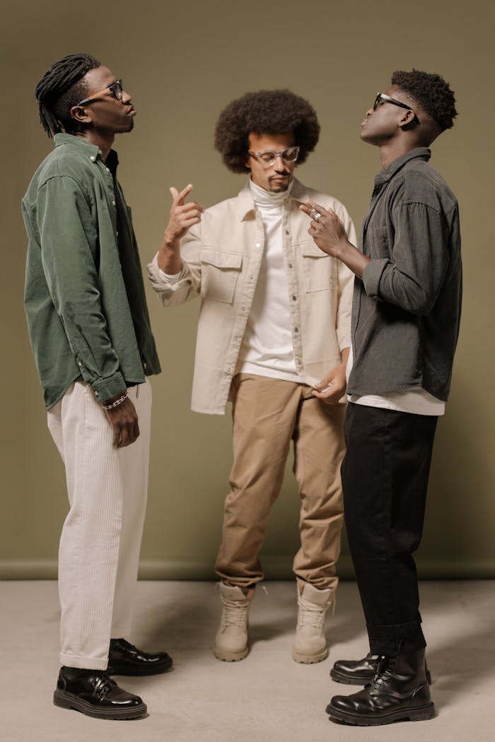 Three men in trendy outfits pose confidently on a neutral backdrop, showcasing modern fashion.