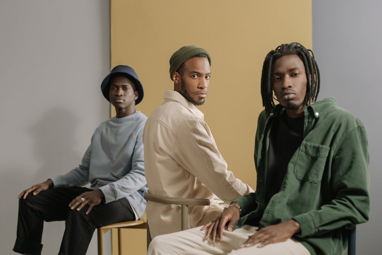 about-us-01 Three stylish men sitting in a minimalist studio with neutral tones and fashionable outfits.